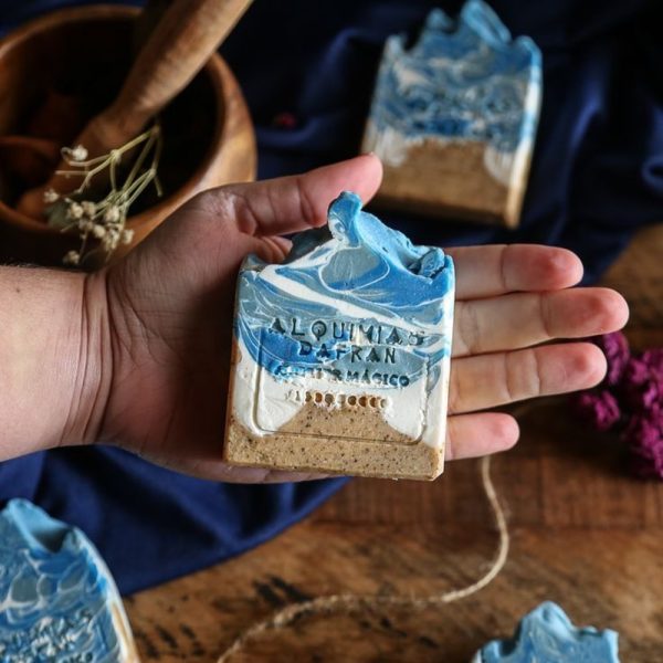 A lavender bath bar held in the hand beside dried flowers